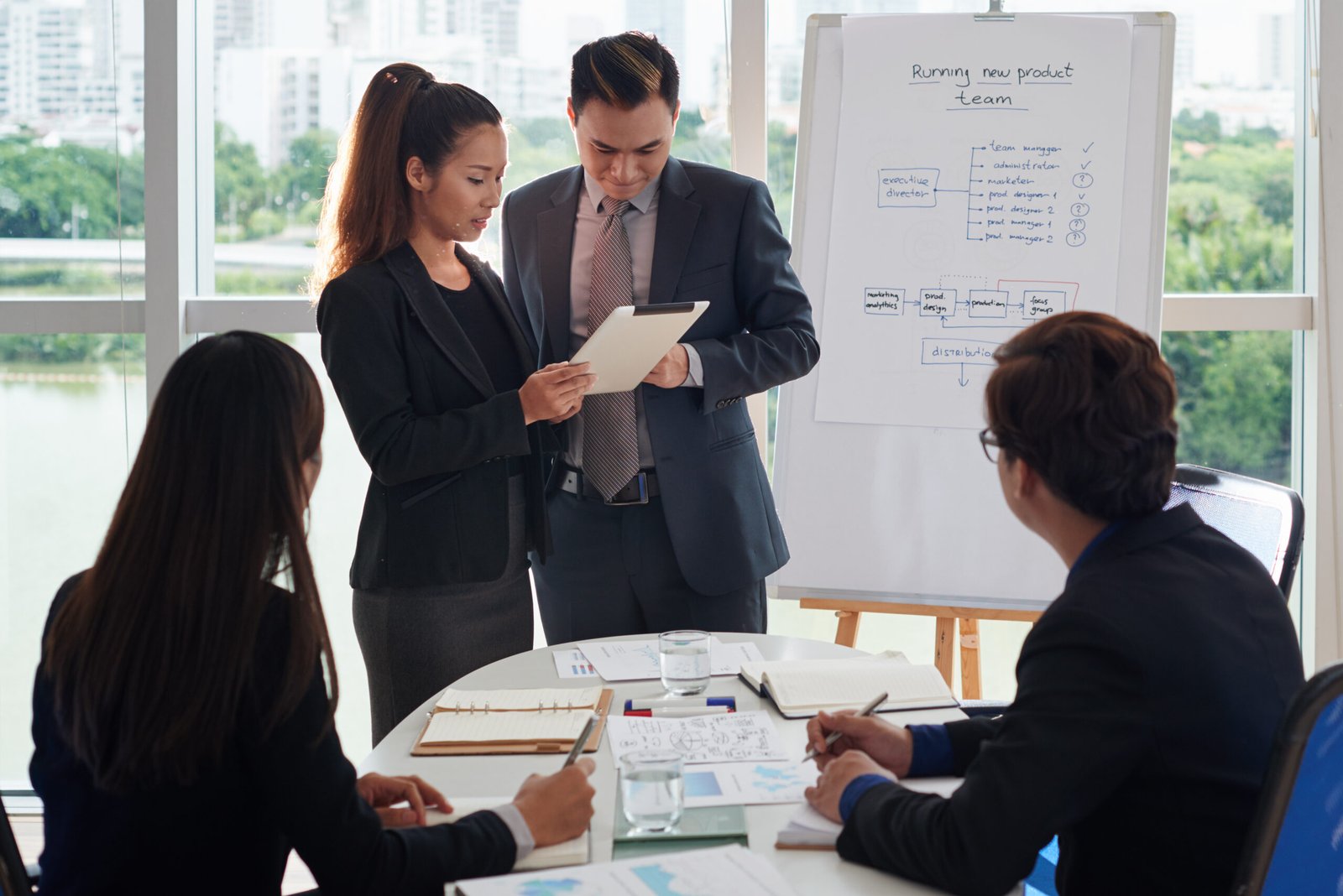 Group of Asian managers gathered together in meeting room and analyzing financial figures, picturesque cityscape on background